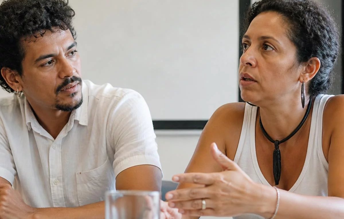Duas pessoas sentadas de frente uma para a outra à mesa: uma fala, a outra registra por escrito